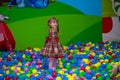 Happy little kid girl in red dress play in pool with colorful plastic balls Royalty Free Stock Photo