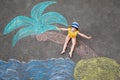 Happy little preschool girl in swimsuit on inflatable ring with sea, sand, palm painted with colorful chalks on asphalt