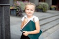 Happy little schoolgirl with book going back to school outdoor.