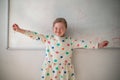 Happy little schoolgirl with down syndrome standing in front of whiteboard and looking at camera Royalty Free Stock Photo