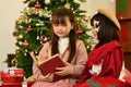 Happy little siblings reading a storybook together in cozy living room decorated for Christmas