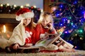 Happy little sisters reading a story book together by a fireplace in a cozy dark living room on Christmas eve Royalty Free Stock Photo