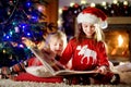 Happy little sisters reading a story book together by a fireplace in a cozy dark living room on Christmas eve Royalty Free Stock Photo