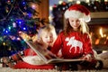 Happy little sisters reading a story book together by a fireplace in a cozy dark living room on Christmas eve Royalty Free Stock Photo