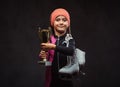 Happy little skater girl champion holds a winner`s cup and ice skates. Isolated on dark textured background. Royalty Free Stock Photo