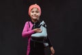 Happy little skater girl dressed in sportswear holds ice skates on a shoulder. Isolated on a dark textured background. Royalty Free Stock Photo