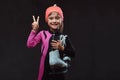 Happy little skater girl dressed in sportswear holds ice skates on a shoulder and shows victory hand. Isolated on dark Royalty Free Stock Photo