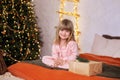 Happy little smiling girl in pajamas with gift on xmas Eve lies on bed. child opens New year gift at home near christmas tree Royalty Free Stock Photo