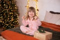 Happy little smiling girl in pajamas with gift on xmas Eve lies on bed. child opens New year gift at home near christmas tree with Royalty Free Stock Photo