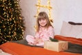 Happy little smiling girl in pajamas with gift on xmas Eve lies on bed. child opens New year gift at home near christmas tree with Royalty Free Stock Photo