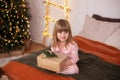 Happy little smiling girl in pajamas with gift on xmas Eve lies on bed. child opens New year gift at home near christmas tree with Royalty Free Stock Photo