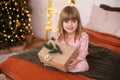 Happy little smiling girl in pajamas with gift on xmas Eve lies on bed. child opens New year gift at home near christmas tree with Royalty Free Stock Photo