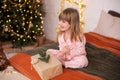 Happy little smiling girl in pajamas with gift on xmas Eve lies on bed. child opens New year gift at home near christmas tree with Royalty Free Stock Photo