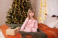 Happy little smiling girl in pajamas with gift on xmas Eve lies on bed. child opens New year gift at home near christmas tree with Royalty Free Stock Photo