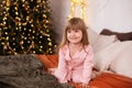 Happy little smiling girl in pajamas with gift on xmas Eve lies on bed. child opens New year gift at home near christmas tree with Royalty Free Stock Photo