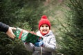 Happy little smiling girl in red cap takes a given box with a gift for Christmas. Kid standing near by spruce. Holiday celebrate