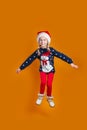 Happy little smiling girl in Santa hat is jumping on orange background. Merry Christmas Royalty Free Stock Photo