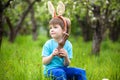 Happy little toddler boy eating chocolate and wearing Easter bunny ears, sitting in blooming garden on warm sunny day. Celebrating Royalty Free Stock Photo