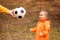 Happy little toddler kid watching at soccer ball in hand of father. Hand of dad giving to little son football ball in autumn park Royalty Free Stock Photo