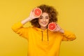 Happy lively energetic woman with fluffy curly hairstyle holding half slice grapefruit and smiling to camera