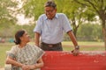 Happy looking retired senior Indian man and woman couple, sitting on a red bench, smiling and looking at each other in a park Royalty Free Stock Photo