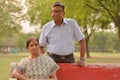 Happy looking retired senior Indian man and woman wearing saree couple smiling sitting on a red park bench in an outdoor setting Royalty Free Stock Photo