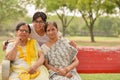 Happy looking young Indian woman with two senior Indian mother / mother in law sitting on a red bench in a park in New Delhi, Royalty Free Stock Photo