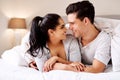 Happy, love and interracial couple in bed together in home holding hands at night. Smile, morning and marriage of an