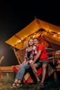 Happy lovely couple relaxing in glamping on evening near cozy bonfire. Luxury camping tent for outdoor recreation and recreation.