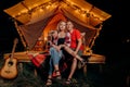 Happy lovely couple relaxing in glamping on evening near cozy bonfire. Luxury camping tent for outdoor recreation and recreation.