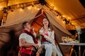 Happy lovely couple relaxing in glamping on summer evening and eating grapes near cozy bonfire. Luxury camping tent for outdoor