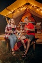 Happy lovely couple with Welsh Corgi Pembroke dog relaxing in glamping on evening and drinking wine near cozy bonfire. Luxury