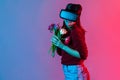 Happy lovely girl in VR glasses headset holding flowers bouquet and smiling flirtatious, playing virtual date