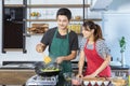 Happy lovely young Asian couple with casual clothes is smiling, helping for preparing and cooking food together in modern kitchen Royalty Free Stock Photo