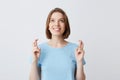 Happy lovely young woman in blue tshirt holding fingers crossed and looking up isolated over white background Feels inspired and Royalty Free Stock Photo