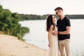 Happy lovers at the beach near lake. Young couple is hugging at sunset on summer day outdoors. A man and woman in love. Concept of Royalty Free Stock Photo