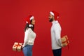 Happy loving arab spouses holding New Year presents behind their backs, exchanging gifts over red studio background