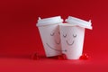 Happy loving couple of emoticons drawn on coffee cups hugging on a red background. Copyspace Royalty Free Stock Photo