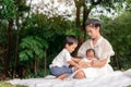 Happy loving family. Asian young beautiful mother and her children, new born baby girl and a boy sitting on green grass to playing Royalty Free Stock Photo