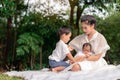 Happy loving family. Asian young beautiful mother and her children, new born baby girl and a boy sitting on green grass to playing Royalty Free Stock Photo