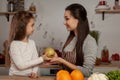 Mother and her daughter are doing a fruit cutting and having fun at the kitchen.