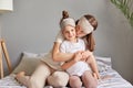 Happy loving family. Mother and her daughter child girl playing and hugging sitting on bed in bedroom woman kissing her cute child Royalty Free Stock Photo