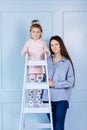 Happy loving family. young Mother and her little daughter standing on blue ladder playing and hugging on blue wall background. Royalty Free Stock Photo