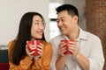 Happy loving japanese spouses sitting on sofa in living room and drinking hot beverage together, enjoying time at home Royalty Free Stock Photo