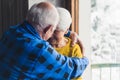 Happy loving senior husband and wife smiling and hugging near the window in the living room at home, enjoying their life Royalty Free Stock Photo