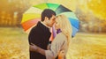 Happy loving young couple kissing and hugging under colorful umbrella in autumn park on warm sunny day Royalty Free Stock Photo