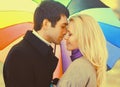 Happy loving young couple kissing and hugging under colorful umbrella in autumn park on warm sunny day Royalty Free Stock Photo