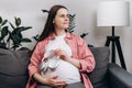 Happy loving young pregnant woman playing classical melody for child by headphones sitting on cozy sofa at home. Unborn baby Royalty Free Stock Photo