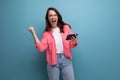 happy lucky brunette woman in informal look with smartphone on studio background