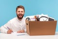 Happy lucky man sitting at workplace with box of belongings and smiling at camera, feeling excited motivated